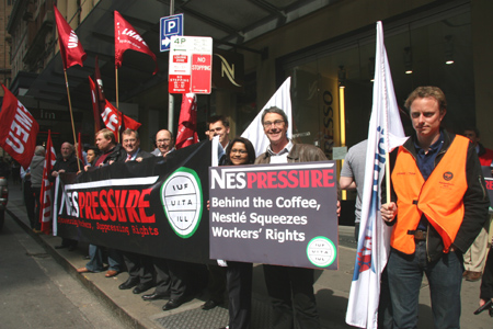 Devant la boutique Nespresso – devant, à droite : James Ritchie tenant une banderole Nespression. Charles Donnelly (président régional UITA-A/P, debout aux côtés de Mark Lennon (avec une  cravate), secrétaire d’Unions NSW. À gauche de la banderole, Neville Donaldson, secrétaire national adjoint de NZ-SFWU.